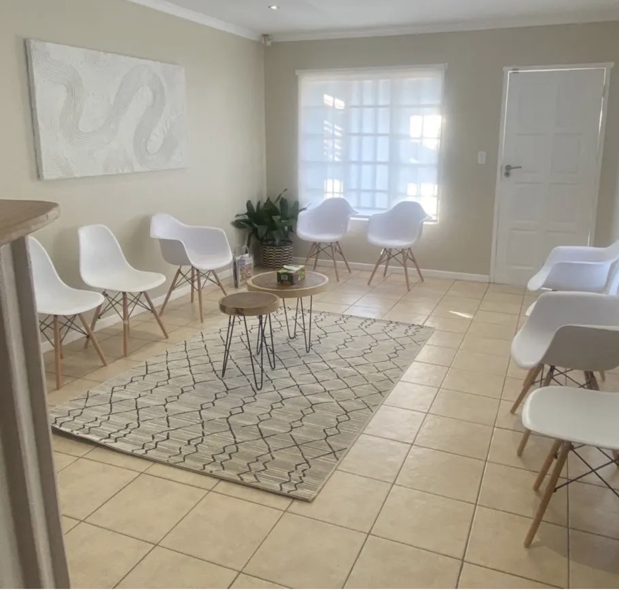 Bright, minimal waiting room with white chairs, a patterned rug and soft natural light